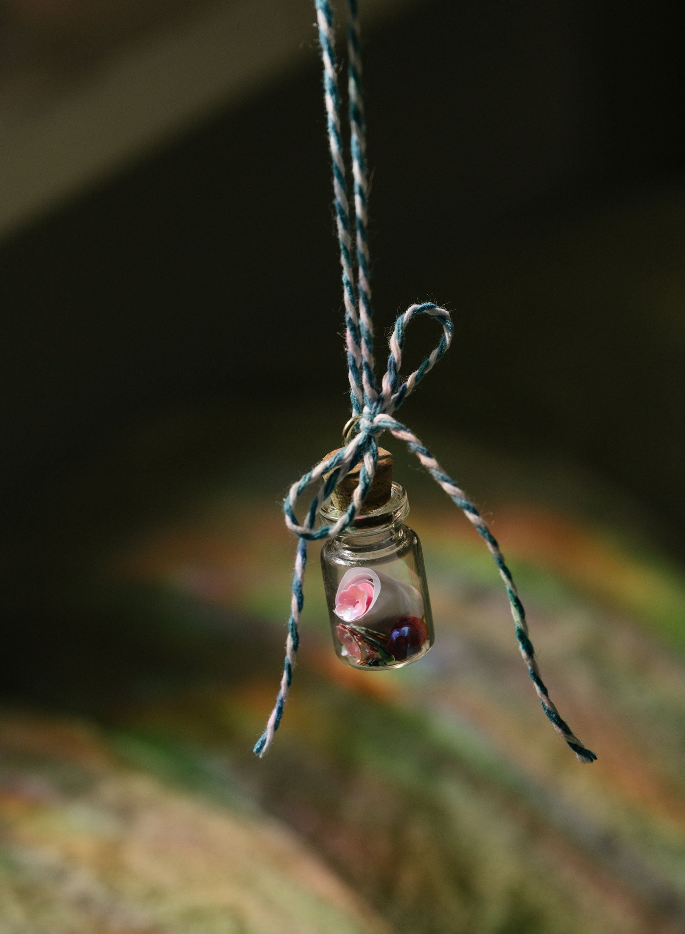 Small glass bottle with a scroll message and glitter inside tied to a string against a blurred natural background
