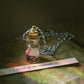 Small glass bottle with a scroll message and glitter inside tied to a string against a blurred natural background
