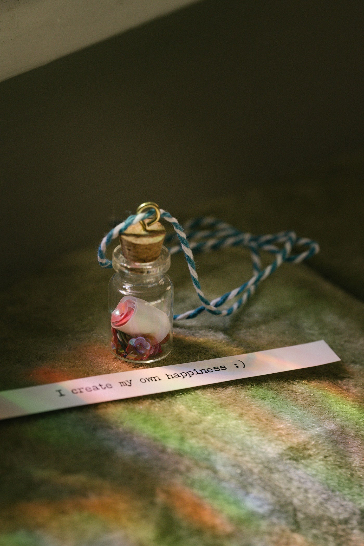 Small glass bottle with a scroll message and glitter inside tied to a string against a blurred natural background